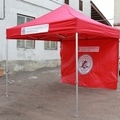 Punainen pop up teltta, jolla on logo katon reunalla sekä seinällä